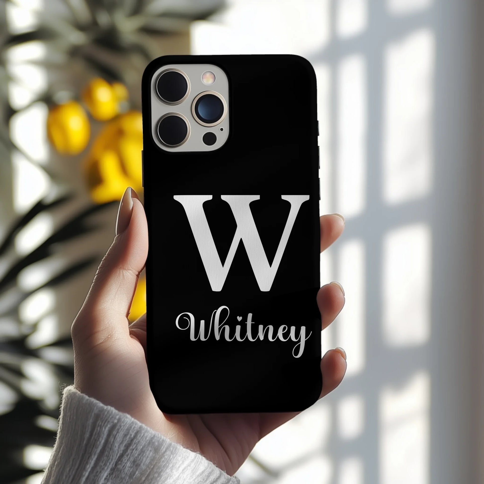 Black phone case with a white 'W' and 'Whitney' text held by a hand.